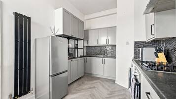 A modern kitchen with stainless steel appliances, white cabinetry, and a herringbone-patterned floor.