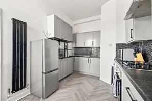 A modern kitchen with stainless steel appliances, white cabinetry, and a herringbone-patterned floor. - Underfloor Heating | Luxury Aberdeen City Centre Apartment 2 Bedrooms (Aberdeen)