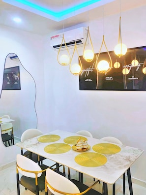 Un espace repas moderne avec une table blanche, des touches dorées et un climatiseur fixé au mur.