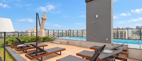 Un área de piscina en la azotea con tumbonas, piscina y vista a la ciudad.
