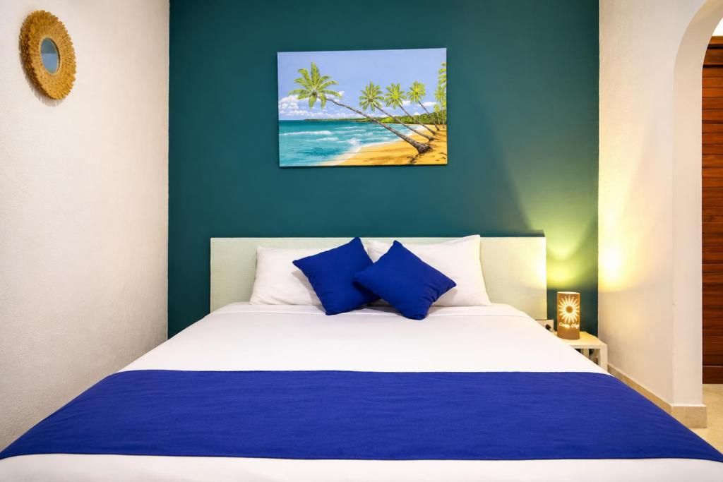 Un lit avec une literie bleue, un tableau représentant une scène de plage et un luminaire fixé au mur.