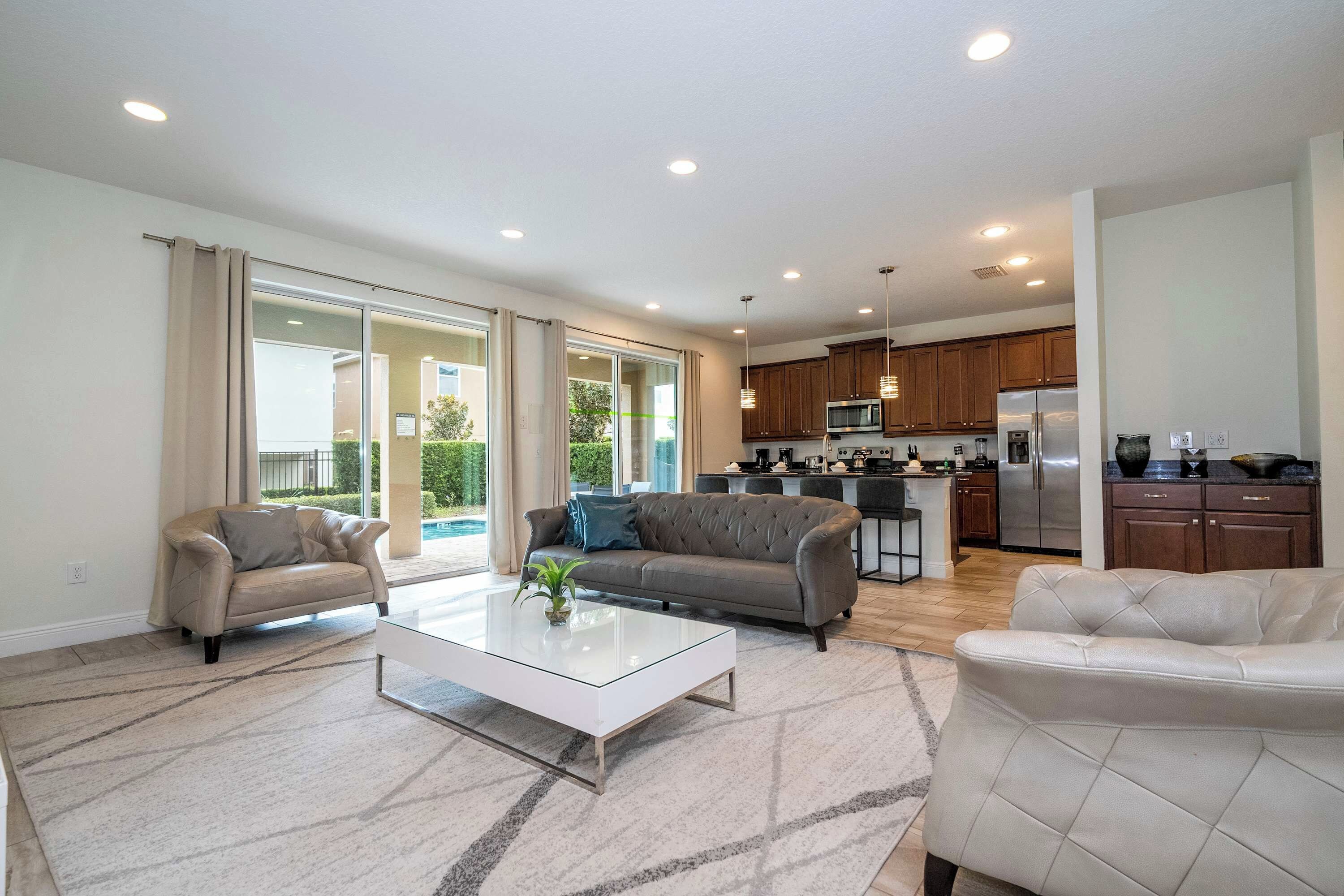 A spacious living room with a glass coffee table, two sofas, and a kitchen in the background.