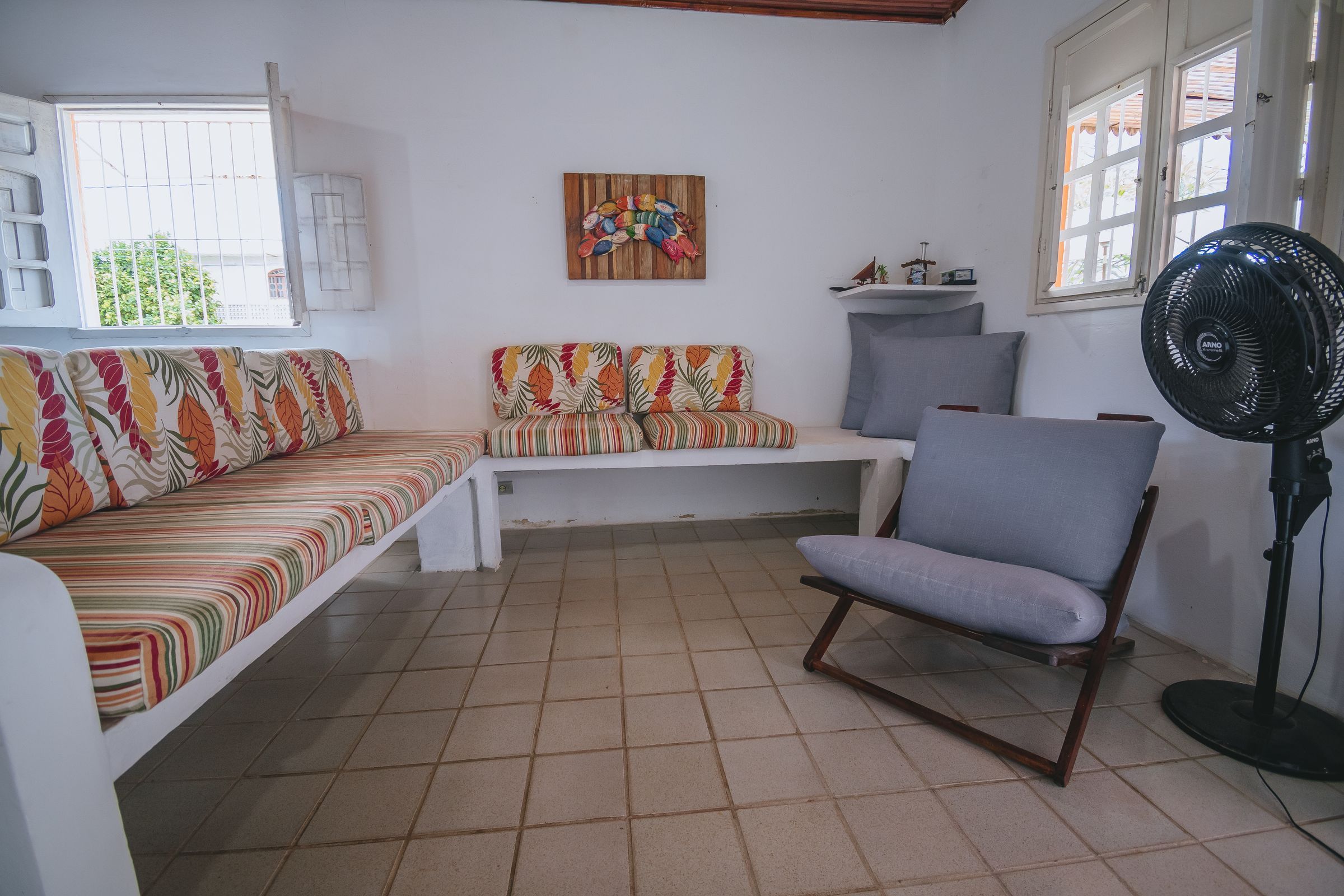 Une pièce comprenant un canapé, un fauteuil, un ventilateur et un tableau accroché au mur.