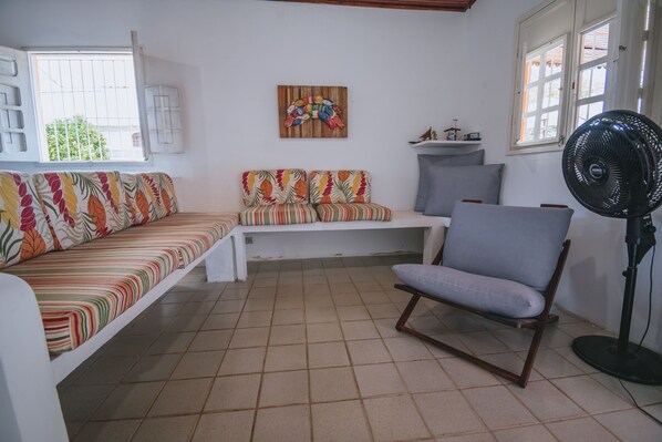 A room with a sofa, a chair, a fan, and a painting on the wall. - Casa com Piscina a 400m da Enseada dos Corais (Cabo de Santo Agostinho)