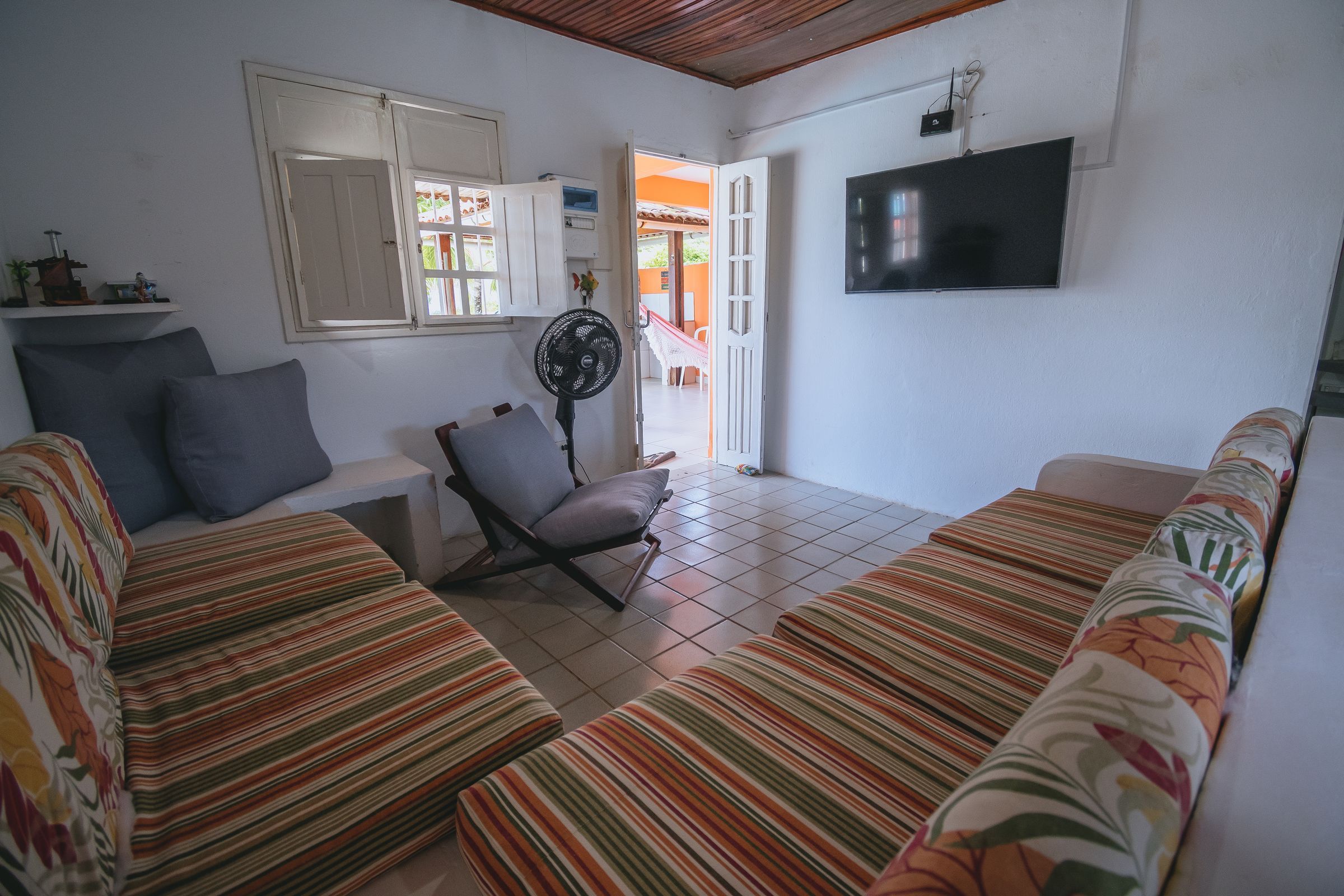 A living room with striped sofas, a chair, a TV, and a fan.