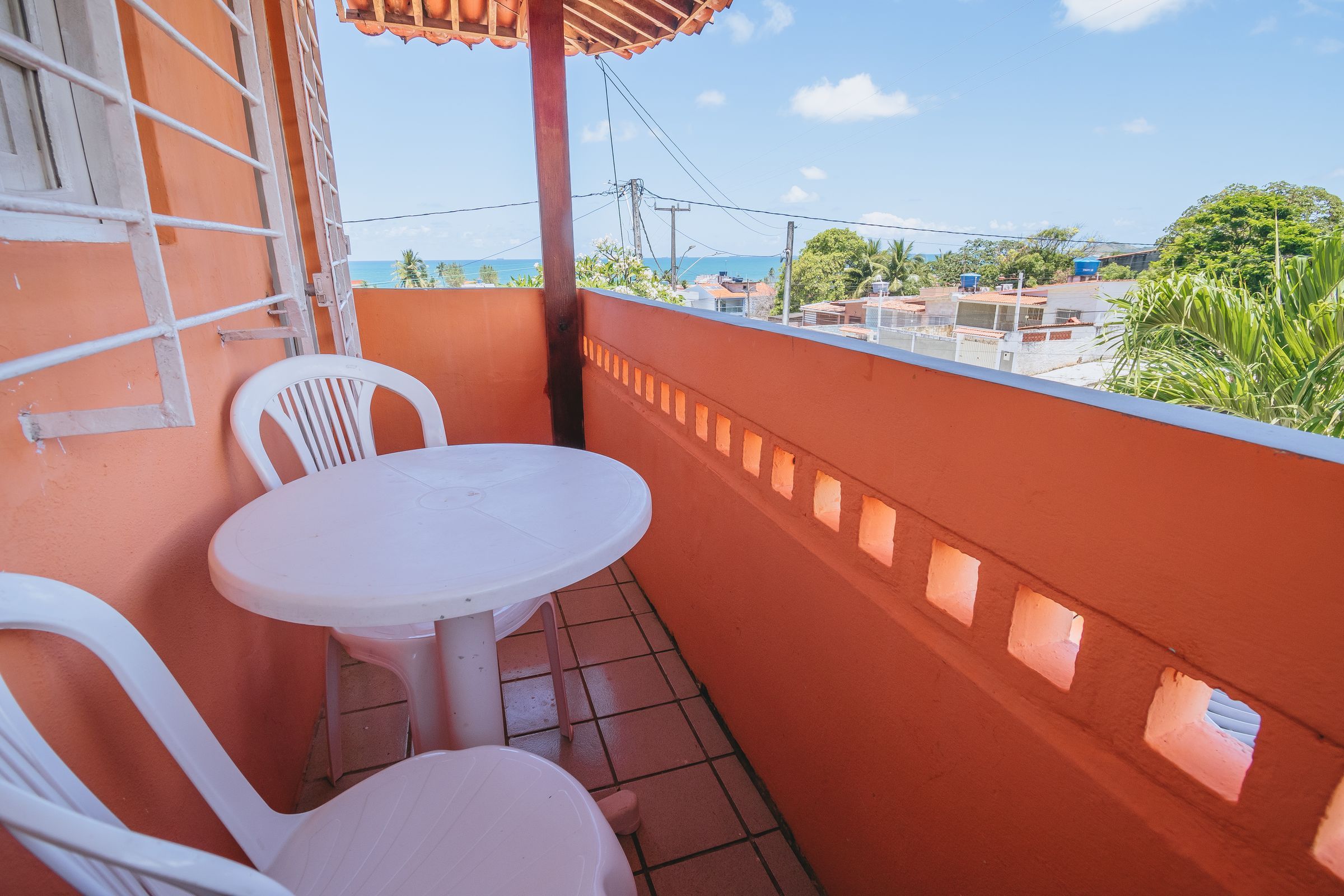 A balcony with a white table and two white chairs, overlooking a residential area with houses and a clear sky.