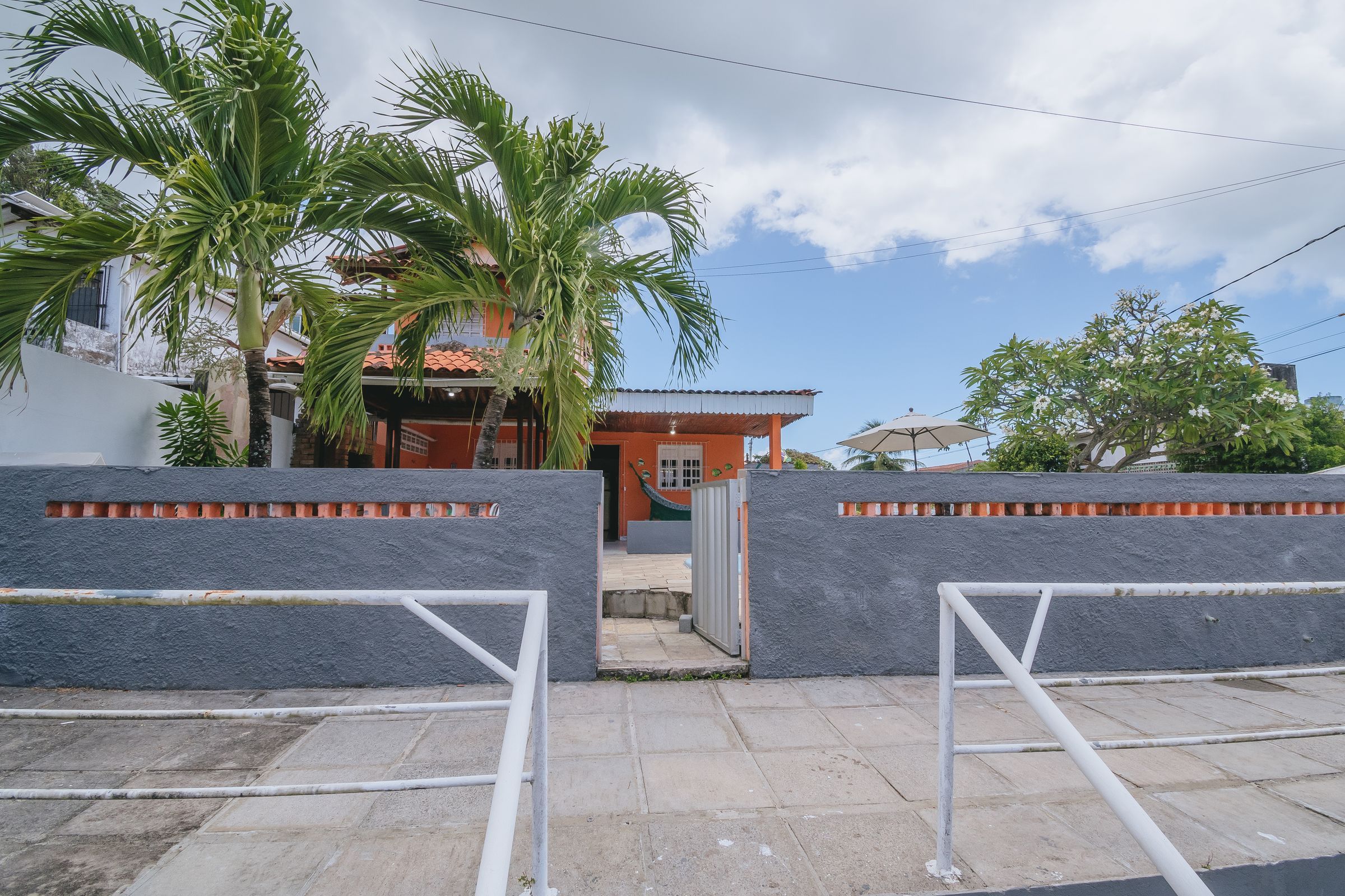 A gated entrance with a paved pathway leading to a building with a red roof and orange walls.