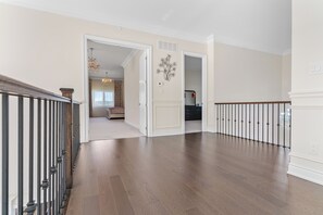 Um corredor amplo com piso de madeira, uma porta branca e uma escada com guarda-corpo preto.