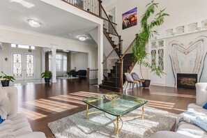 Amplia sala de estar con una mesa de centro de vidrio, una escalera y una chimenea.
