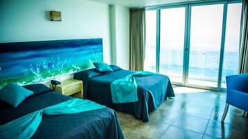 Quarto de hotel com duas camas, uma janela grande e vista para o mar.