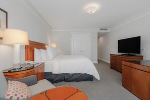 Ett hotellrum med en säng, sänglampor, ett skrivbord med en telefon, en tv och en sittgrupp med en stol och kuddar.