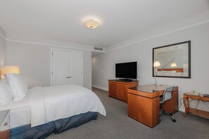 Une chambre d’hôtel avec un lit, un bureau et une chaise, une télévision et un miroir au mur.