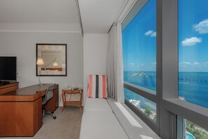 Une chambre d’hôtel équipée d’un bureau, d’une chaise et d’une grande fenêtre donnant sur la mer et un pont.