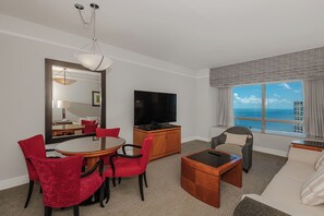 Une chambre d’hôtel comprenant un coin repas, une télévision, un canapé et une grande fenêtre donnant sur un beau paysage.