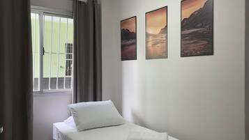 Ein Schlafzimmer mit einem Einzelbett, einem Deckenventilator und drei Landschaftsbildern an der Wand.