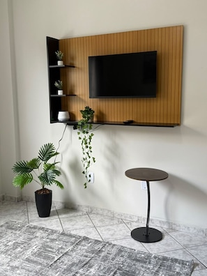 Una sala moderna con televisor montado, una planta en maceta, una mesita y suelo de baldosas.