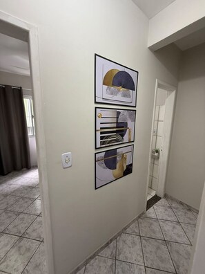 A hallway with a tiled floor, a door, and three framed abstract artworks on the wall. - Temer & fasolo ltda (Vitória)