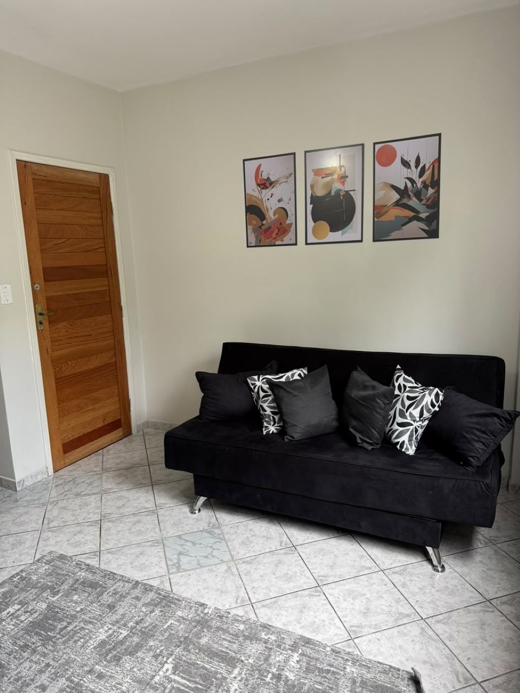Un sofá negro con cojines estampados, una puerta de madera y un cuadro abstracto en la pared.