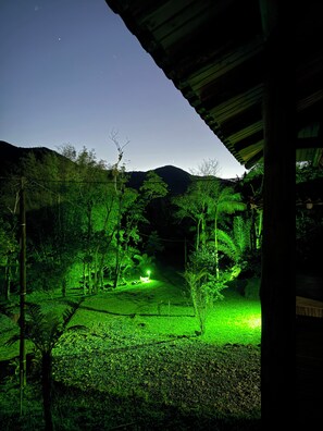 A nighttime view of a rural area with a path leading to a house, surrounded by trees and hills. - Estância 3 por 1 (Guaratuba)