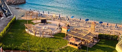 An aerial view of a beachside resort with a circular seating area, sun loungers, and a small building.