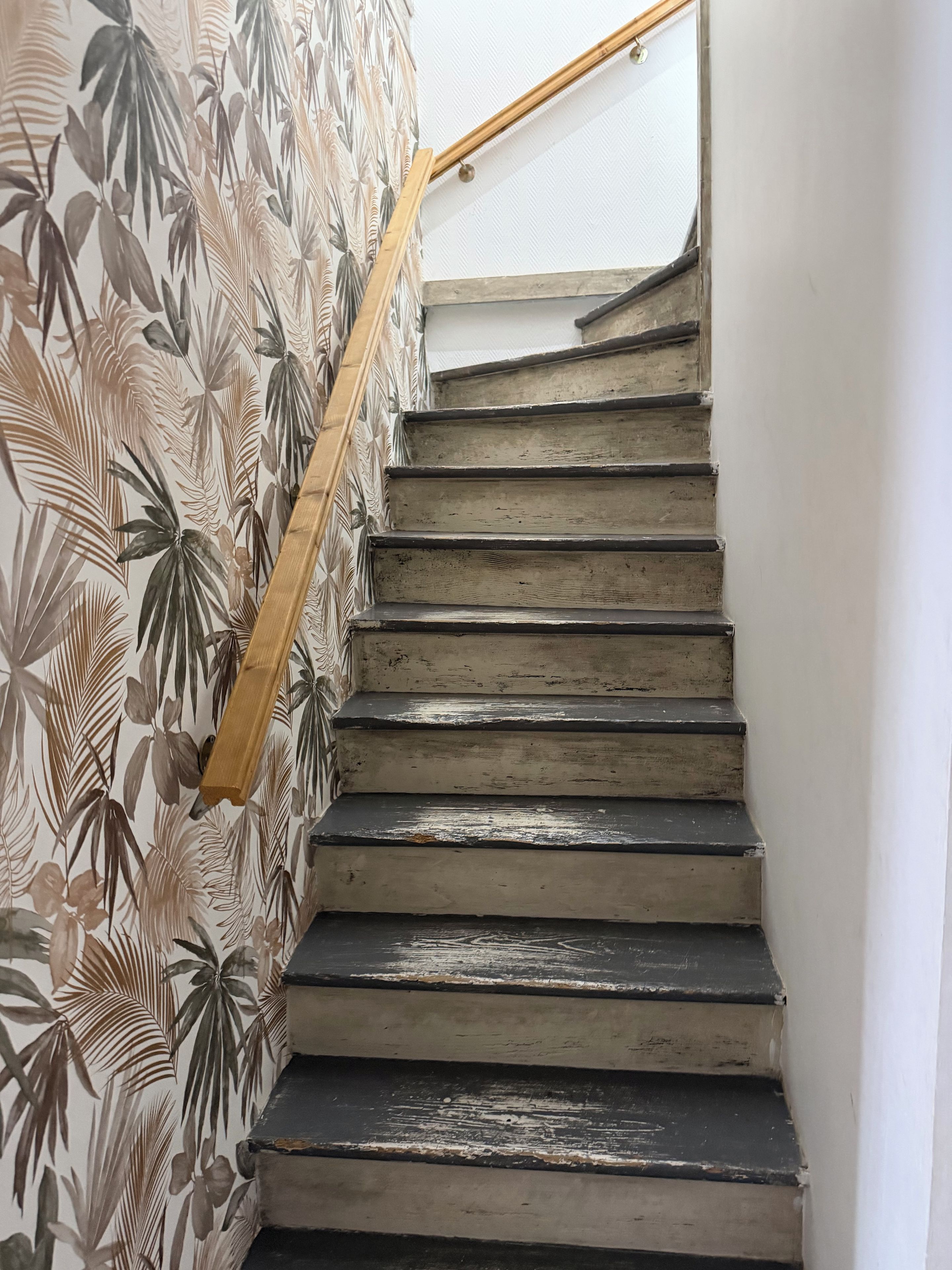 A staircase with a wooden handrail and a wall with a tropical leaf pattern.