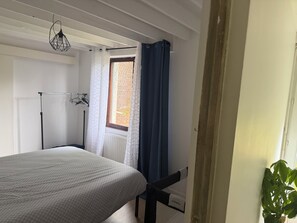 A bedroom with a bed, a window with curtains, a radiator, and a hanging light fixture. - New Listing (Récourt)