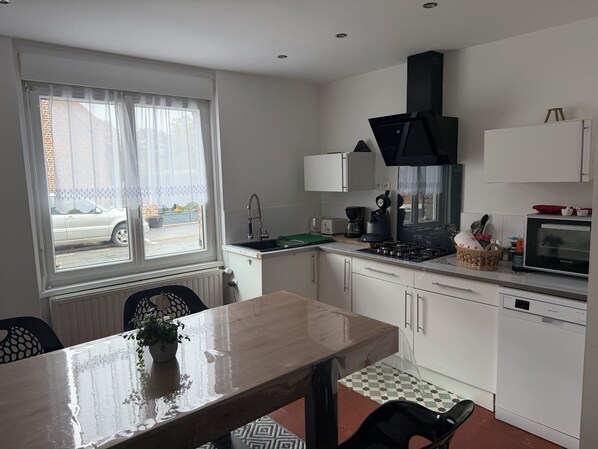 A compact kitchen with a window, a dining table, and basic appliances. - New Listing (Récourt)