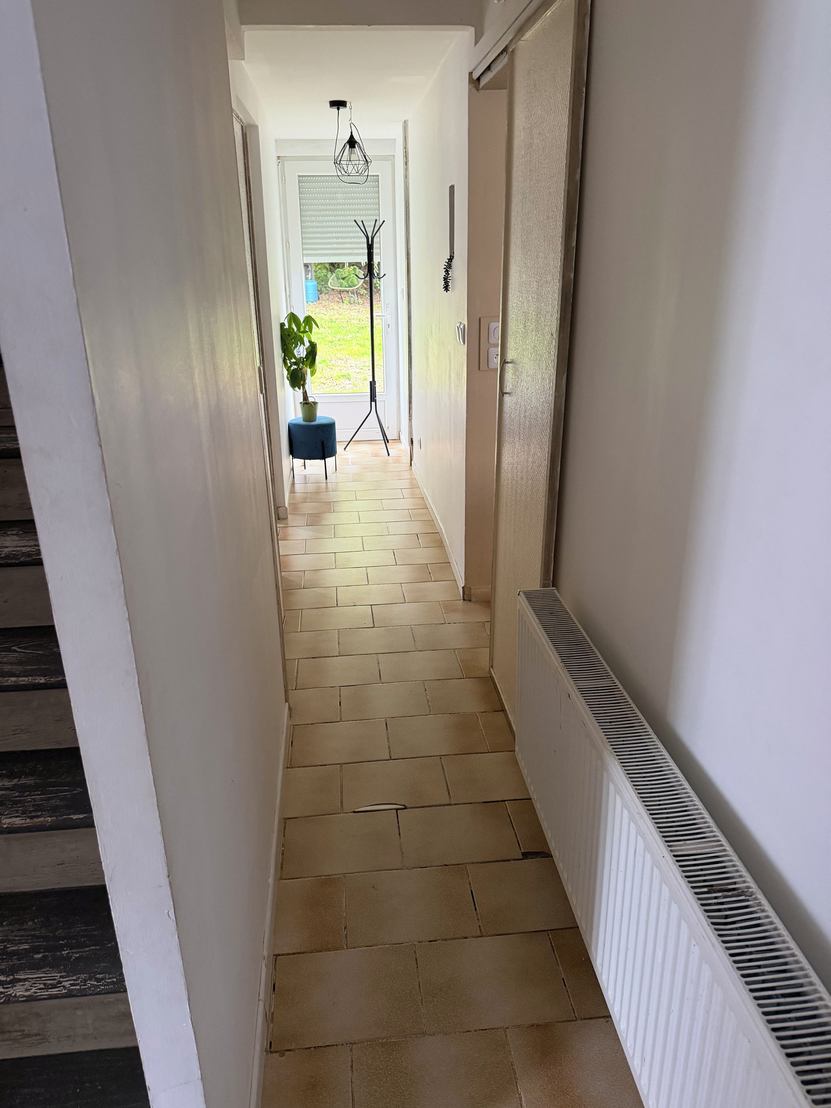 A hallway with a radiator, a potted plant, and a tripod with a light.