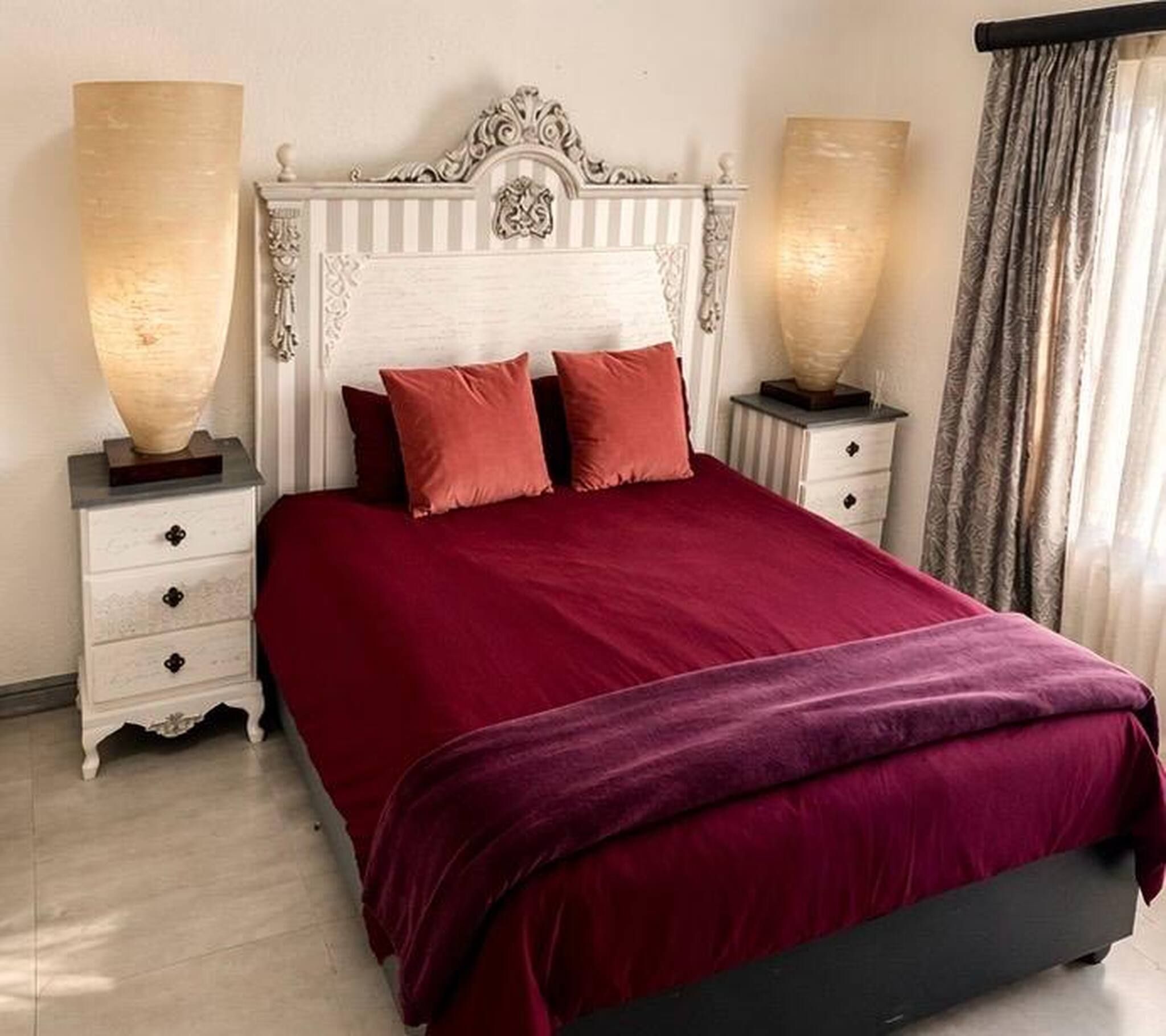 A bed with a white headboard and red bedding, flanked by two bedside tables with lamps.
