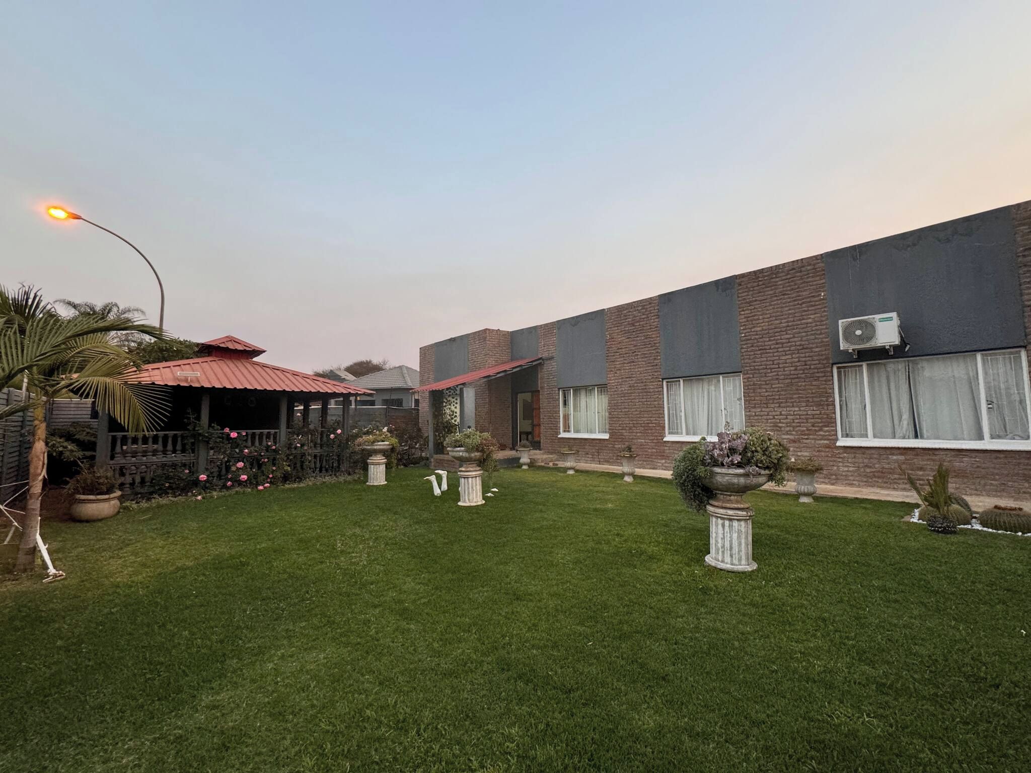 A building with a brick facade, a red roof, and a well-maintained lawn with potted plants.
