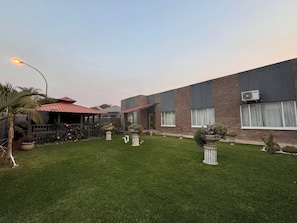 A building with a brick facade, a red roof, and a well-maintained lawn with potted plants. - Hansoty Airbnb Ivypark Polokwane (Polokwane)