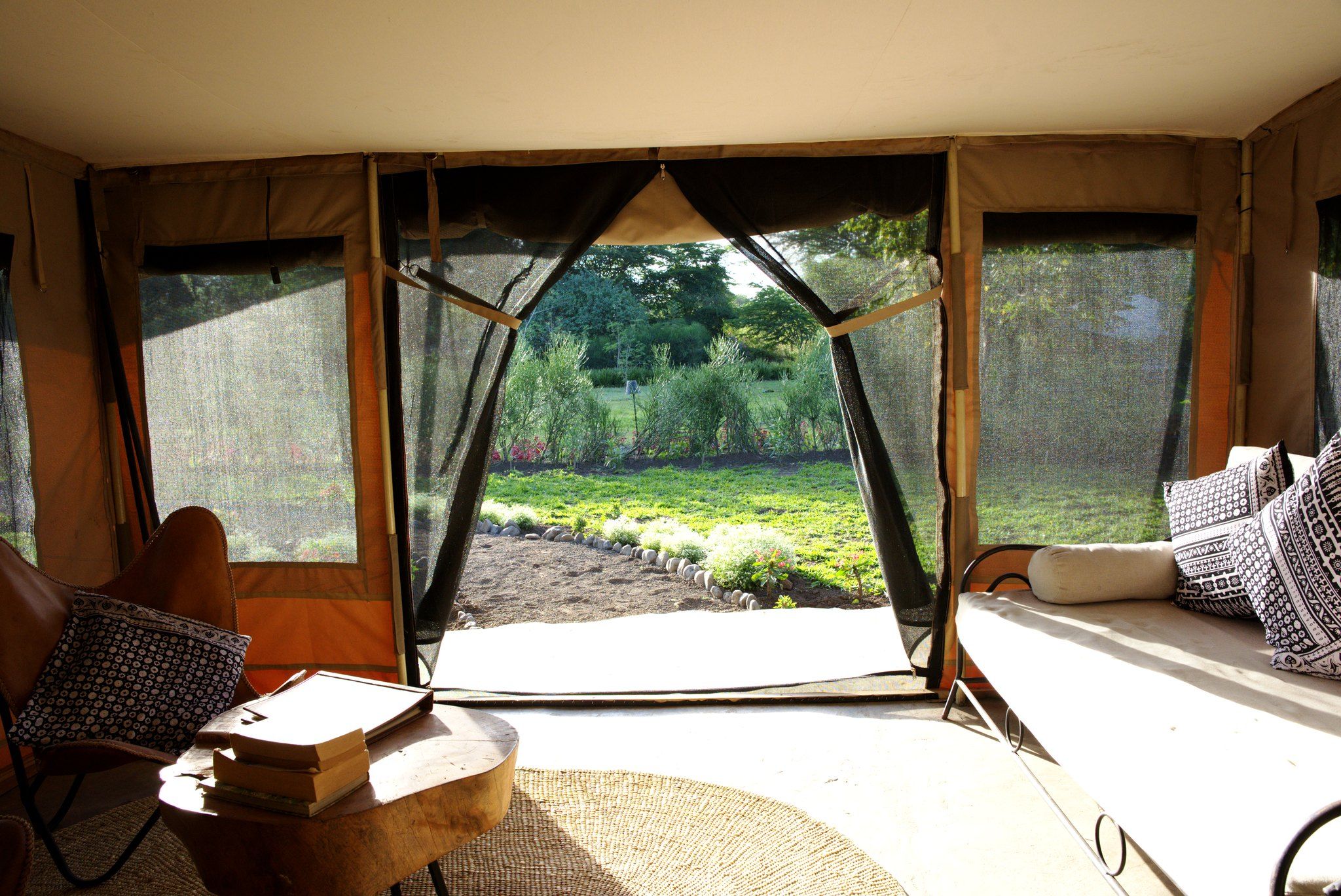 A tented room with a view of a garden, a table with books, and two chairs.