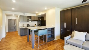 Una cocina moderna con una isla central, un comedor con un taburete de bar y una sala de estar con sofá y un mueble grande.