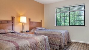 Une chambre d’hôtel avec deux lits, une table de chevet avec une lampe et une fenêtre avec des stores.