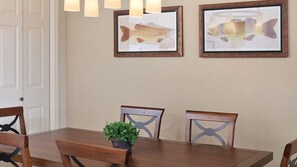 Un coin repas avec une table en bois, des chaises et deux tableaux représentant des poissons, accrochés au mur.