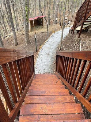 A wooden staircase leading to a covered area in a wooded setting. - Poplar Cottage at Saluda River Farms (Greenville)