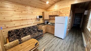 A compact kitchen with wooden cabinets, a microwave, a refrigerator, and a sofa with a table.