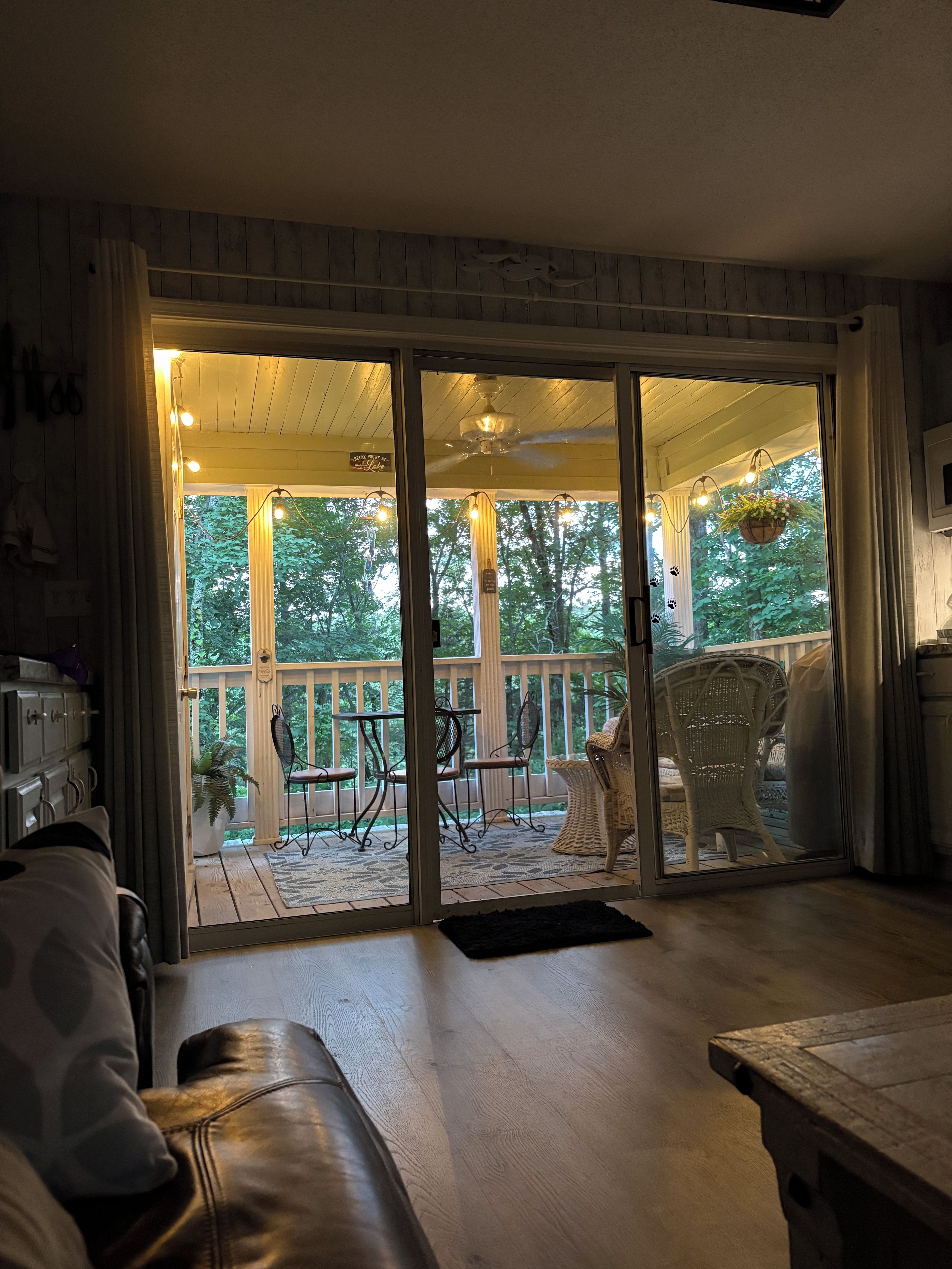 A room with a sliding glass door leading to an outdoor patio area with wicker furniture and a view of trees.