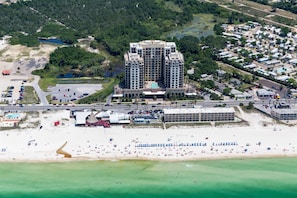 Un hotel moderno con piscina, cerca de una playa con numerosas sombrillas.