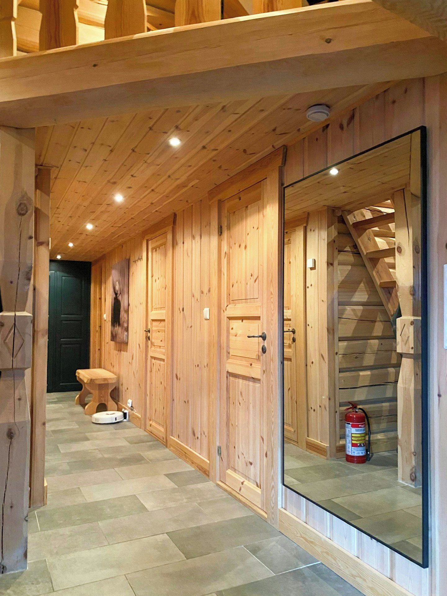 A wooden hallway with a bench, a fire extinguisher, and a staircase.