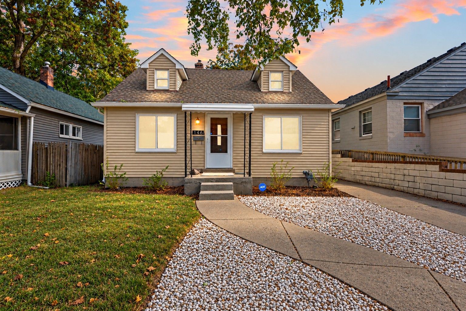 A two-story house with a front porch, a driveway, and a gravel pathway leading to the entrance.