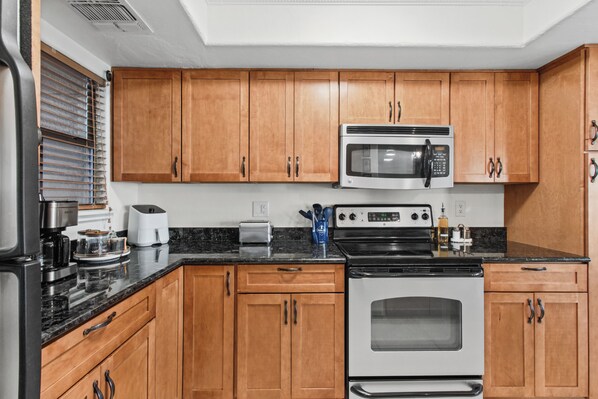 A kitchen with wooden cabinets, a microwave, a toaster, a coffee maker, and a stove. - Foothill Garden | Pool, Patio & La Encantada (Tucson)