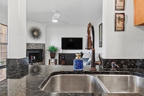 A modern kitchen with a double sink, a ceiling fan, and a flat-screen TV in the background. - Foothill Garden | Pool, Patio & La Encantada (Tucson)