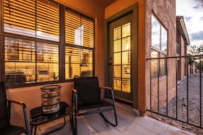 A balcony with two chairs and a table, a door with a window, and a view of the street. - Foothill Garden | Pool, Patio & La Encantada (Tucson)