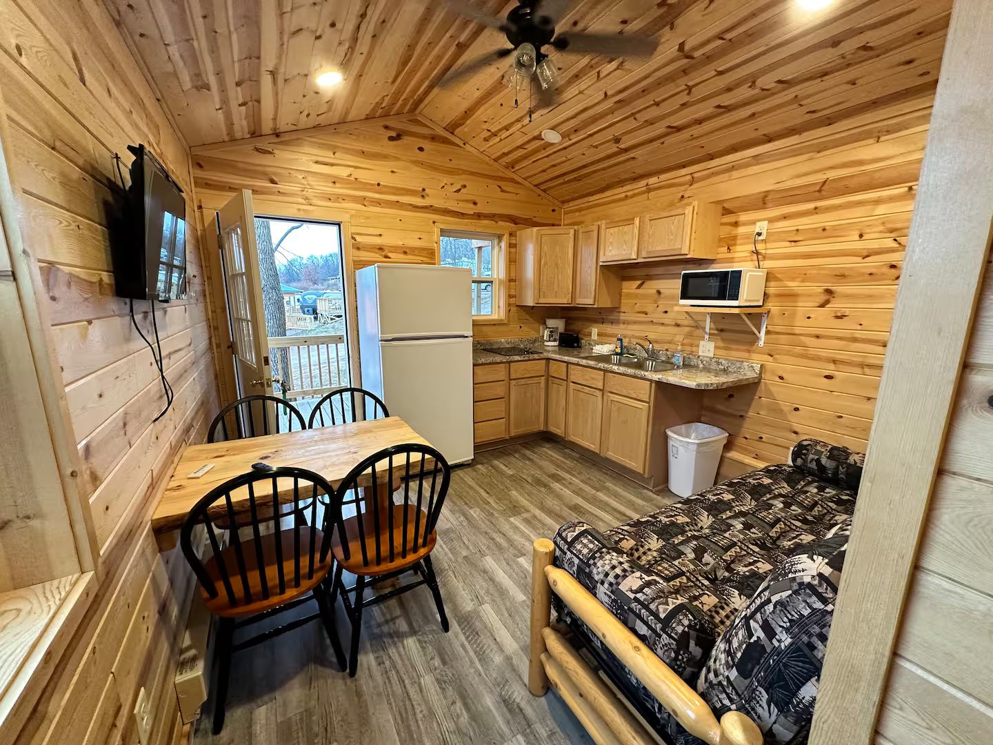 A compact wooden cabin with a dining area, kitchenette, and a bed.