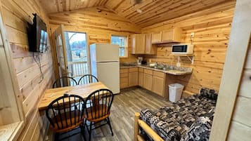 A compact wooden cabin with a dining area, kitchenette, and a bed.