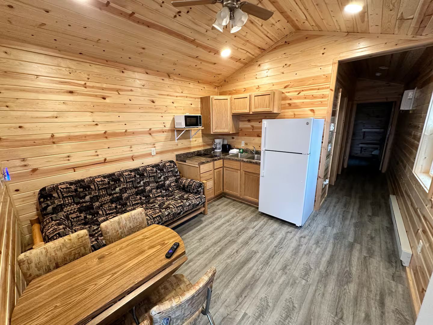 A compact kitchen with wooden cabinets, a microwave, a refrigerator, and a sofa with a table.