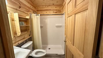 A wooden-paneled bathroom with a toilet, sink, and shower stall.