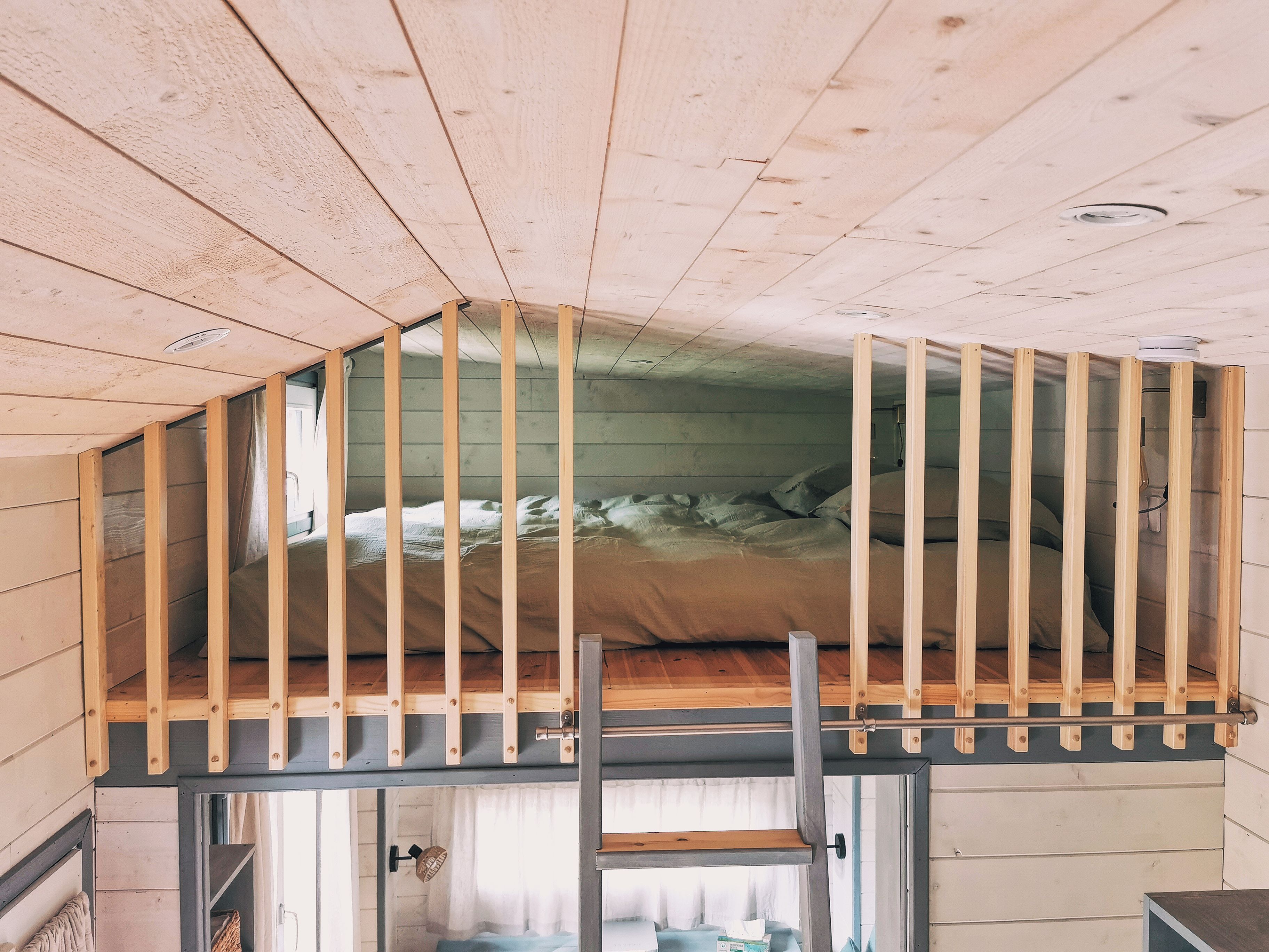 A loft bedroom with a wooden bunk bed, a window with curtains, and a door leading to another room.