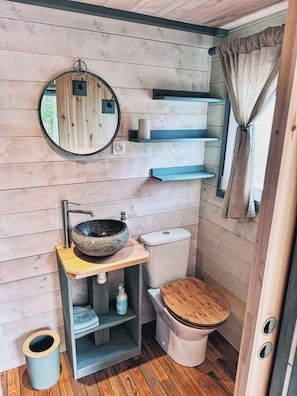 Un baño pequeño con tocador de madera, espejo redondo, inodoro y ventana con cortinas.